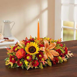 Low floral centerpiece with a sunflower, orange lily, and orange taper candle