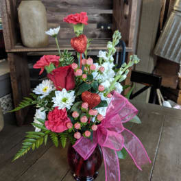 Pink and white floral arrangement in a red glass vase with a pink bow