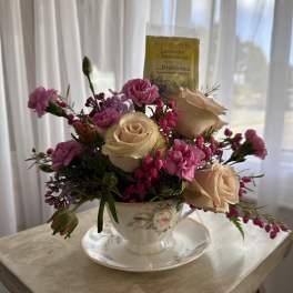 Pink and cream roses arranged in a teacup with a tea packet behind them.