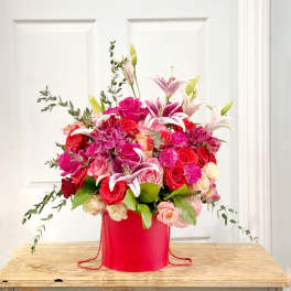 Pink and red floral arrangement in a red hatbox