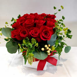 Red roses arranged in a white box with greenery and a red ribbon