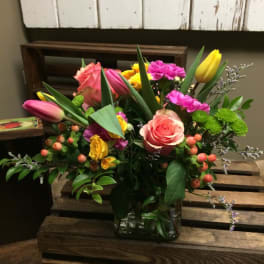 Mixed bouquet of pink roses, tulips, and yellow blooms in a glass vase