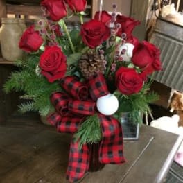 Red roses arranged with plaid ribbon and holiday accents in a vase