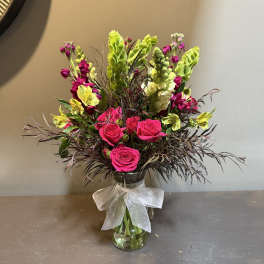 Bright pink roses and yellow flowers in a clear glass vase with a white bow