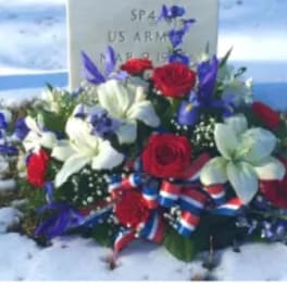 Patriotic red, white, and blue floral spray with ribbon placed at a snowy grave marker