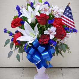Red roses and white lilies in a vase with a blue ribbon and small American flag