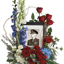 Floral memorial frame with red roses, blue and white flowers, and a black-and-white portrait