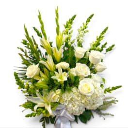 White roses and lilies arranged with green accents and a silver ribbon