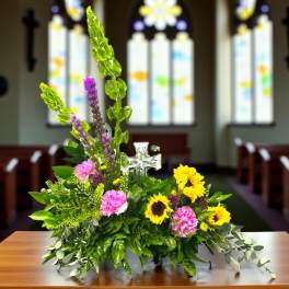 Floral church arrangement with sunflowers, pink carnations, and a clear cross pick