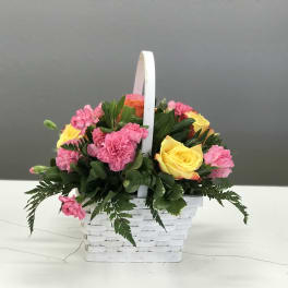 Pink carnations and yellow roses in a white basket