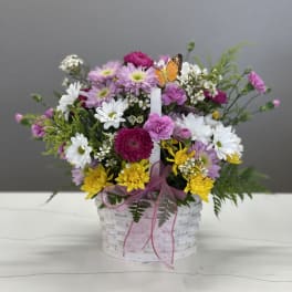 Mixed bouquet in a white basket with pink ribbon and a butterfly pick