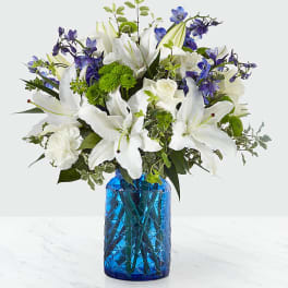 White lilies and blue flowers in a blue glass vase