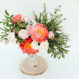 Pink and white floral arrangement in a clear vase on a wood slice base