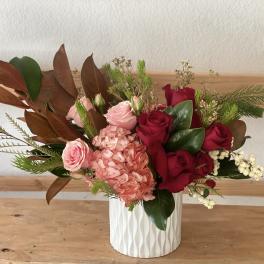 Pink and red roses in a white textured vase with mixed greenery