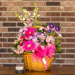Pink and purple mixed flowers in a wicker basket with a bright ribbon