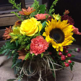 Mixed bouquet with a sunflower, yellow rose, and pink carnation in a rustic container