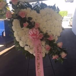 Heart-shaped standing wreath of white flowers with pink roses and a pink ribbon on an easel