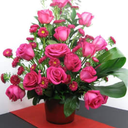 Tall arrangement of hot pink roses and small pink asters in a red pot on a red table runner
