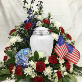 Memorial floral arrangement around a white urn with red, white, and blue flowers