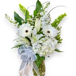 White floral arrangement in a glass vase with a ribbon bow