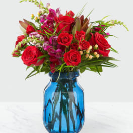Red roses and pink flowers arranged in a blue glass vase