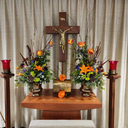 Symmetrical floral altar arrangement with orange lilies and roses beside a crucifix