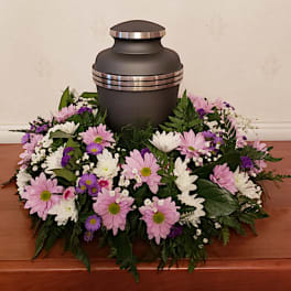 Funeral urn surrounded by a pink, white, and purple floral wreath