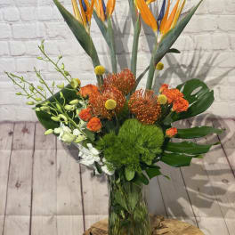 Tropical bouquet with bird of paradise, orange roses, and green filler in a glass vase