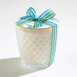 White candle in a textured glass jar with a floral lid and blue-green ribbon bow.