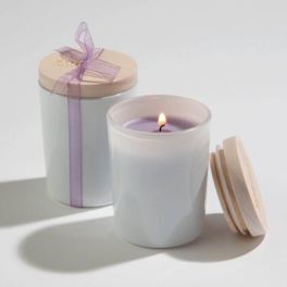 Pair of white glass jar candles with wooden lids, one lit and one tied with a lavender ribbon