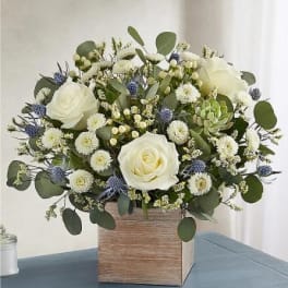 Compact arrangement of white roses and button flowers with blue accents in a wooden cube vase