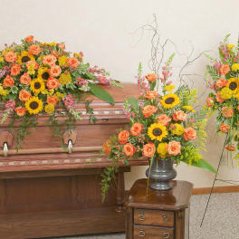 Sympathy set with orange roses and yellow sunflowers on a casket, in a vase, and on a standing spray.