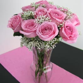 Arrangement of pink roses with white filler flowers in a clear glass vase