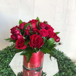 Round arrangement of red roses in a glass cylinder vase on a mirrored base