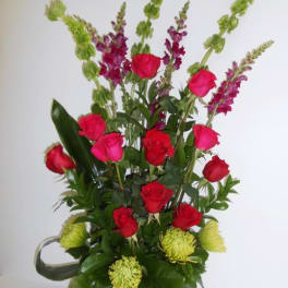Tall bouquet of red and pink roses with green and purple spikes in a black vase