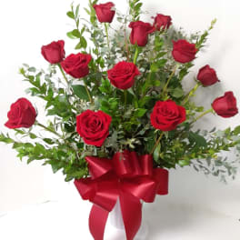 Red roses arranged in a white vase with a red ribbon bow