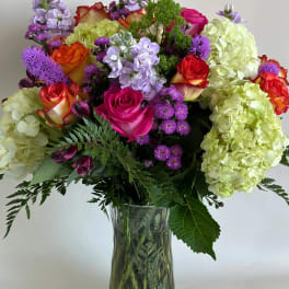 Mixed bouquet of roses, hydrangeas, and purple flowers in a glass vase