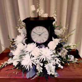 White floral arrangement around a black clock on a wooden table