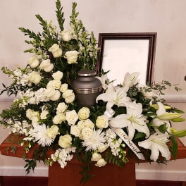 White funeral spray with roses and lilies around an urn