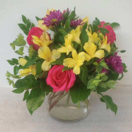 Mixed bouquet of pink roses, yellow alstroemeria, and purple daisies in a glass vase