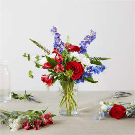 Mixed bouquet of red, white, and blue flowers in a clear glass vase