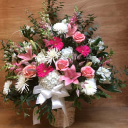 Pink and white mixed flower arrangement in a basket with a white ribbon