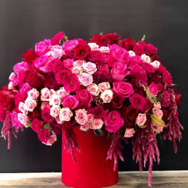 Large arrangement of pink and red roses in a red cylindrical vase
