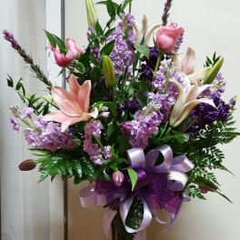 Pink lilies and purple flowers in a glass vase with a lavender ribbon