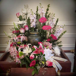 Pink and white funeral spray on a casket with a memorial ribbon