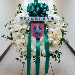 White funeral wreath with lilies, roses, and a green ribbon bow