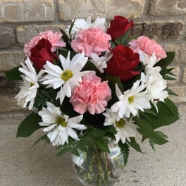 Bouquet of red roses, pink carnations, and white daisies in a glass vase