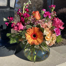 Bright mixed bouquet in a round glass vase with orange and pink blooms