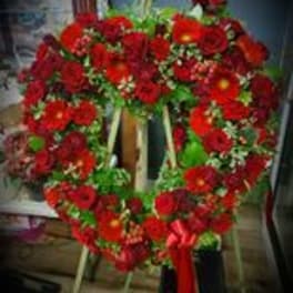 Heart-shaped standing wreath of red flowers with a red ribbon bow on an easel