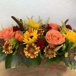 Autumn floral arrangement with roses, daisies, and small pumpkins in a low container